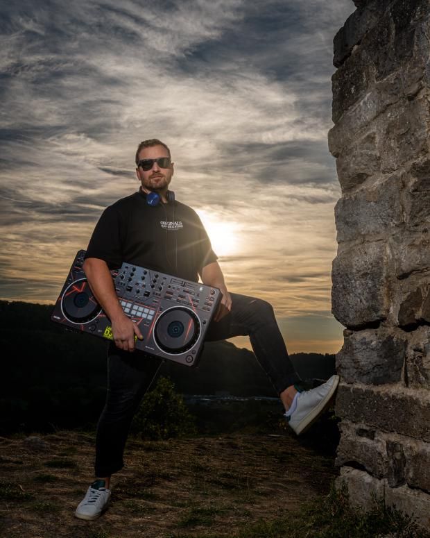 DJ Jannis mit DJ-Controller im Arm vor einer Burgruine bei Sonnenuntergang über dem Kochertal