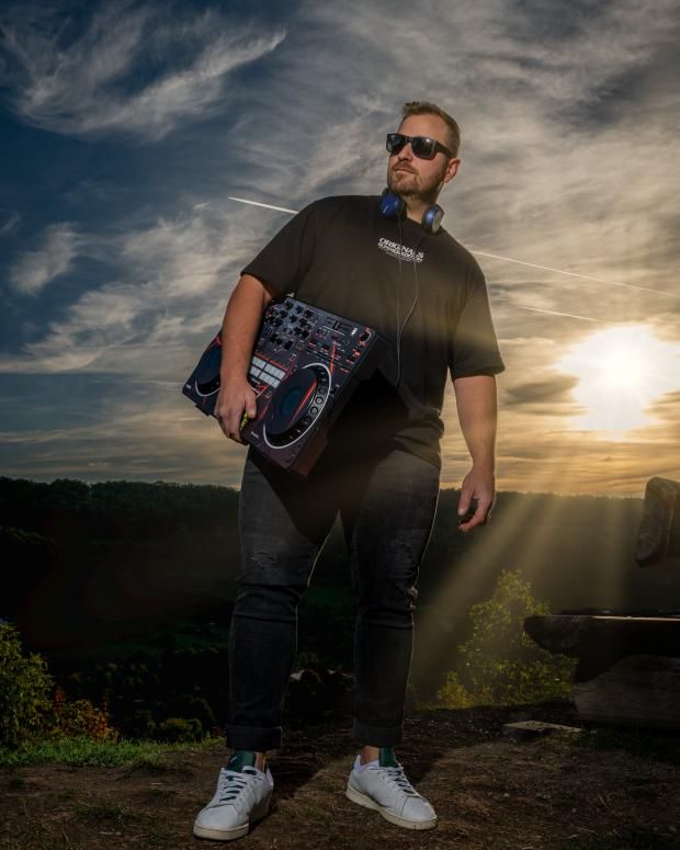 DJ Jannis mit DJ-Controller und Kopfhörern auf einer Anhöhe bei Schwäbisch Hall im Gegenlicht der Abendsonne