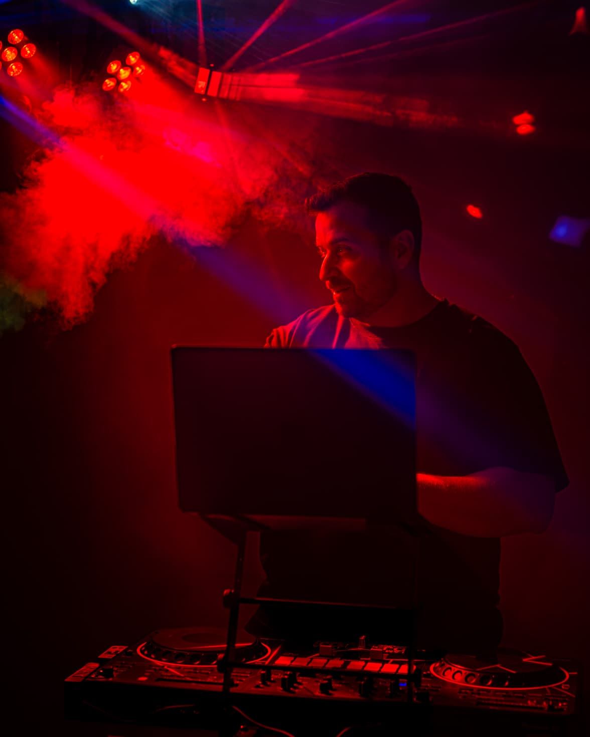 DJ Jannis hinter dem Pult im Club, rote Lichtstrahlen und Nebel